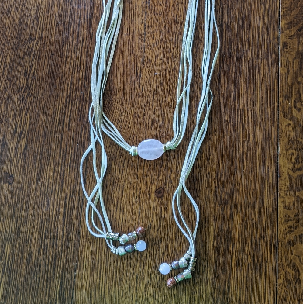Lariat style faux leather strand necklace. Accented with pink stone, beads